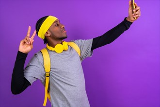 Black ethnic man with backpack and yellow headphones on a purple background