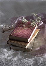 Three closed books with glasses and babys breath on white fur with pink cloth