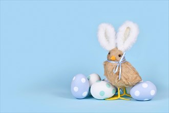 Easter chick with bunny ears and pastel Easter eggs on blue background with copy space