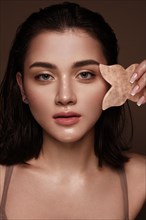 Beautiful young girl with natural nude make-up with gua sha for facial massage in hands. Beauty face. Photo taken in studio