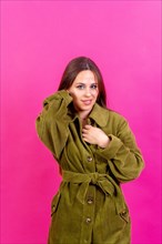 Close up portrait of a young caucasian woman in green trench coat isolated on the pink background
