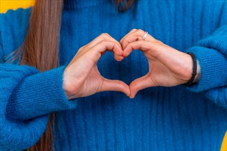Young brunette woman wearing blue sweater over isolated yellow background smiling in love making heart symbol shape with hands. romantic concept
