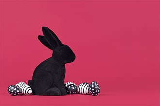 Black and white easter eggs with hearts and stripes next to bunny figure on pink background
