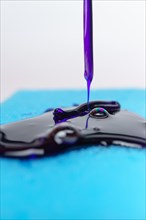 Purple liquid soap dripping on a blue sponge on a white background