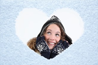 Woman looking through a snow heart on a window pane