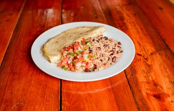 Gallopinto dish with quesillo and pico de gallo on wooden table. Traditional Gallo Pinto Meal with Pico de Gallo and quesillo served