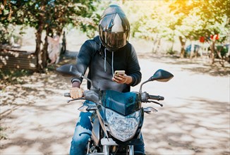 Man on motorbike texting while driving. Motorcyclist on motorcycle using cell phone outdoors. Concept of distracted motorcyclist with cell phone