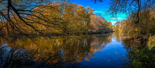 Panorama of the river Leine in autumn with trees with colourful leaves and blue sky