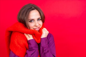 Beautiful young woman with warm red scarf on red background. cold winter portrait