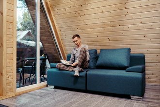 Middle aged man sits with book on sofa at chalet