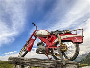 An old rusty red motorcycle stands on a wooden pole
