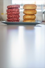 Stack of raw beef burgers with their buns on a mirrored white plate