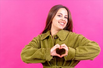Young brunette woman wearing green sweater over isolated pink background smiling in love making heart symbol shape with hands. romantic concept