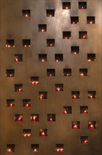 Burning sacrificial candles in a metal wall