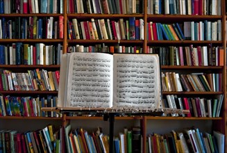 Sheet music and flute on a music stand in front of a wall of books