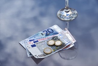 Empty wine glass with Euro banknotes and coins on a glass top cafe table