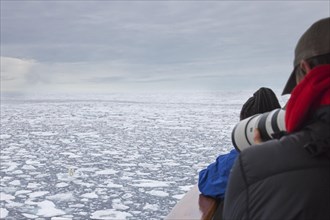 Eco-tourists taking pictures of lone polar bear from ship on drift ice