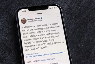 Smartphone with a Twitter tweet from Donald Trump with a message about his conspiracy theories