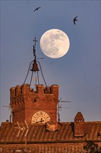 Full moon over Pienza in Tuscany in front of the historic tower of the town hall with tower clock