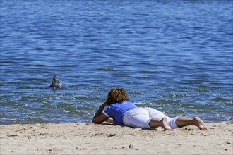 Woman lying on her belly on the beach watching grey seal bottling