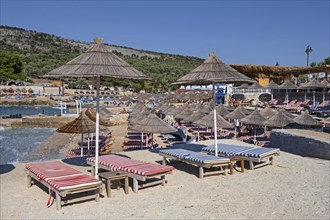 Parasols and sunloungers on sandy beach at seaside resort Ksamil along the Albanian Riviera in summer
