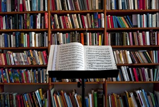 Sheet music on a music stand in front of a wall of books