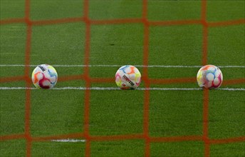 Three adidas Derbystar match balls lie on turf behind goal net