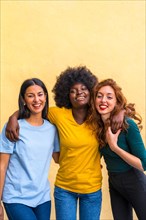 Portrait of beautiful multiethnic female friends smiling on a yellow wall having fun, copy paste