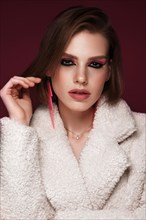 A beautiful young woman in a white fur coat with bright pink make-up and earrings. Beauty face. Photo taken in the studio