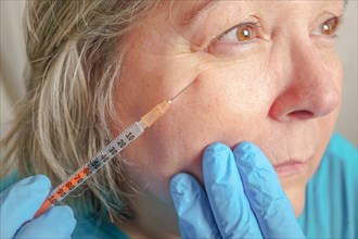Close-up of a cosmetologists hands injecting botox into the face of an older woman with wrinkles