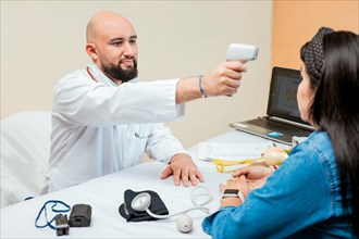Doctor measuring temperature with infrared gun to female patient, Doctor taking temperature to woman patient in office, Male doctor taking temperature with gun to patient