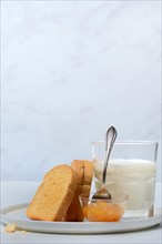 Rusk, glass of milk and orange marmalade in small bowls