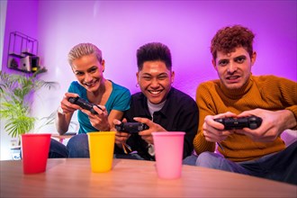 Group of young friends playing video games together on the sofa at home, smiling, young millennials