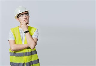 Concept of a meditative engineer solated. Pensive builder man with hand on chin, Portrait of young builder thinking with hand on chin isolated, A pensive engineer on white background