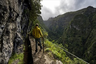 Hikers on a narrow path along a levada, view of forested mountains, Levada do Caldeirao Verde, Parque Florestal das Queimadas, Madeira, Portugal, Europe