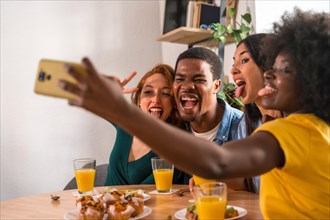 Multiethnic friends at a breakfast with orange juice and muffins at home, selfie smiling