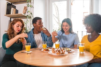 Multiethnic friends at a breakfast with orange juice and muffins at home, detail cutting the toasts