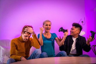 Group of young friends playing video games together on the sofa at home, purple led, woman winning