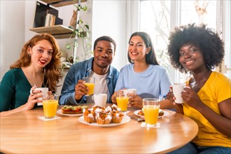 Multiethnic friends having breakfast with orange juice and muffins at home