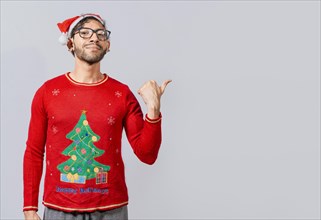 Friendly Christmas man pointing to a space to the side. Friendly smiling young man in christmas clothes pointing at a promo. Cheerful christmas man concept pointing promo offer isolated
