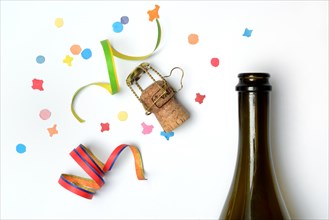 Champagne bottle, champagne cork, streamers and confetti against a white background