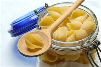 Conchiglie, shell pasta in glass container with cooking spoon, pasta