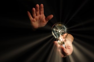 Man holding in his hands a lighted light bulb with rays of light on a black background
