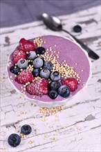 Fruit smoothie bowl with yogurt decorated with healthy raspberry, blueberry and puffed quinoa grain on iron tray