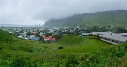 Village view of Vik in the rain, lava beach with Reynisdrangar rock needles in the back, Vik, Iceland, Europe