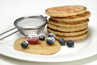 Blini, stacked blinis and sieve with icing sugar, fruit, mini pancakes