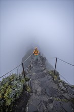 Hiker on a narrow slope in the fog, Pico Arieiro to Pico Ruivo hike, hiking trail on rocky cliff, Central Mountains of Madeira, Madeira, Portugal, Europe