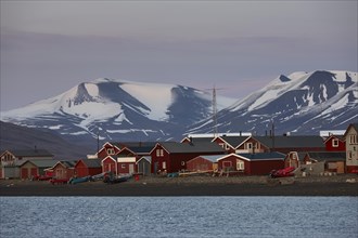 Red fishermens huts and wooden houses on the beach, glaciated mountain peaks behind, evening mood, Longyearbyen, Spitsbergen