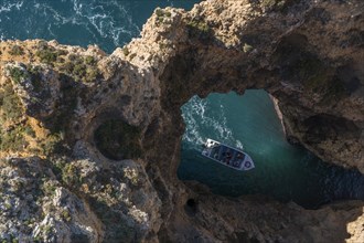 Boat going into a cave at Praia da Marinha, rocks and cliffs, steep coast in the Algarve, Portugal, Europe