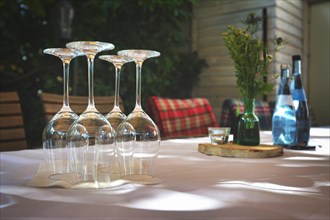 Elegant table at restaurant with arranged empty wine glasses turned upside down and blurry background with water bottles, table decoration and chairs with blankets